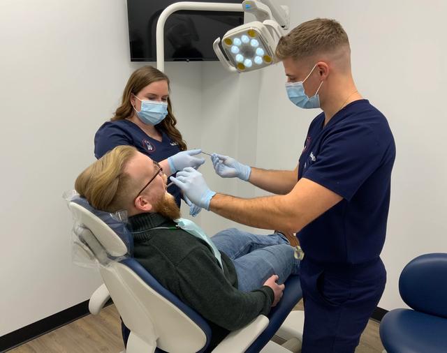 a man is sitting in a dental chair getting his teeth examined by two dentists .