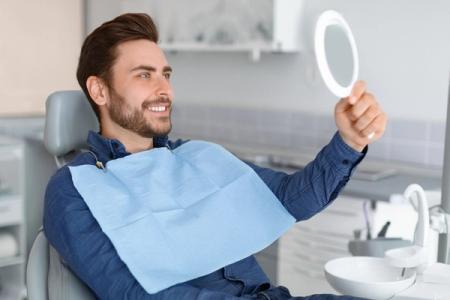 a man is sitting in a dental chair looking at his teeth in a mirror .