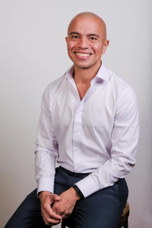 un hombre en camisa blanca está sentado en un taburete y sonriendo