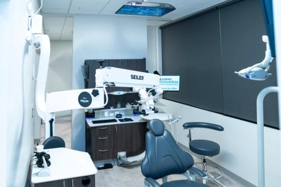 A modern endodontic treatment room with a dental chair, a Seiler microscope, and a monitor for Lower Columbia Endodontics.