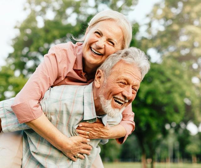 a man is giving a woman a piggyback ride in a park .