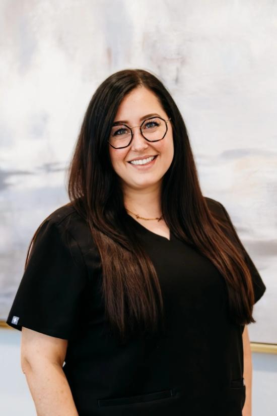 a woman wearing glasses and a black scrub top is smiling for the camera .