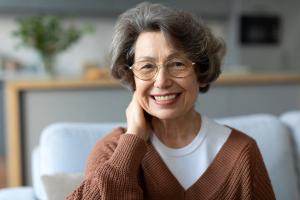 an elderly woman wearing glasses is smiling while sitting on a couch .