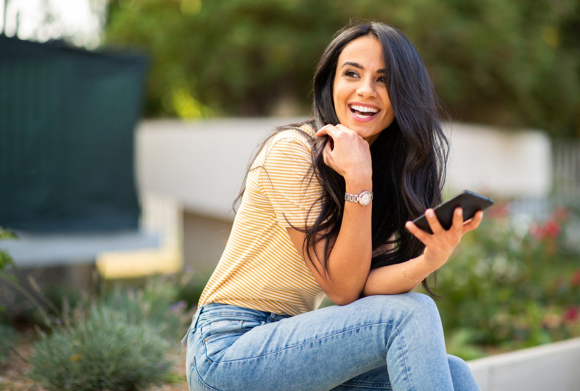 a woman is sitting on a curb holding a cell phone and smiling .