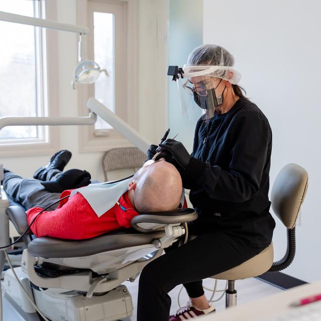 a man is laying in a dental chair getting his teeth examined by a dentist .
