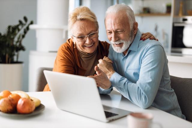 an elderly couple is sitting at a table looking at a laptop computer .