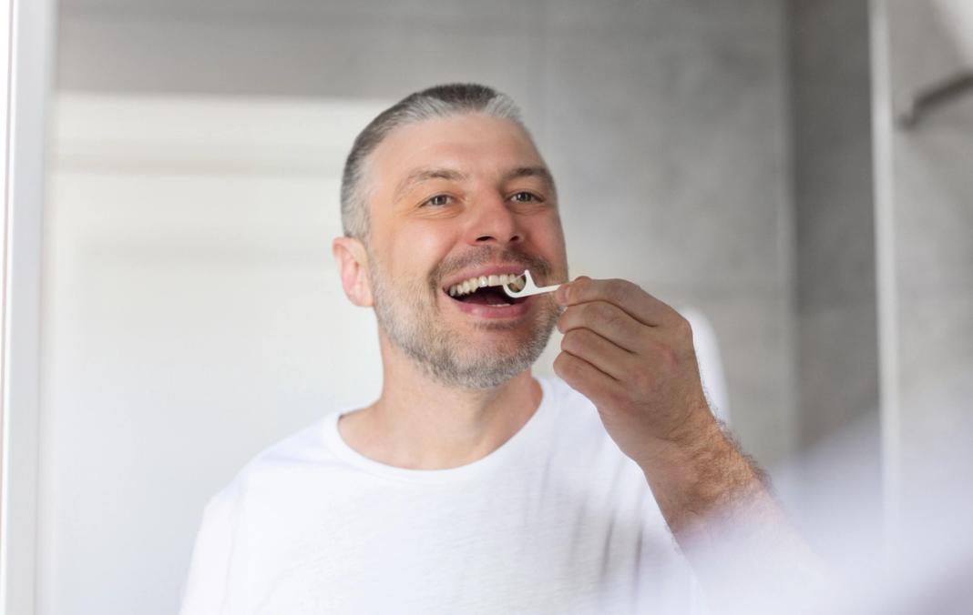 a man is flossing his teeth in front of a mirror .