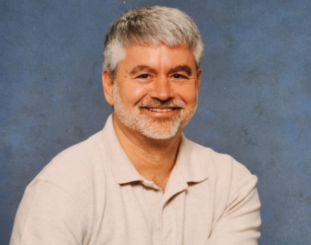 a man with gray hair and a beard smiles for the camera