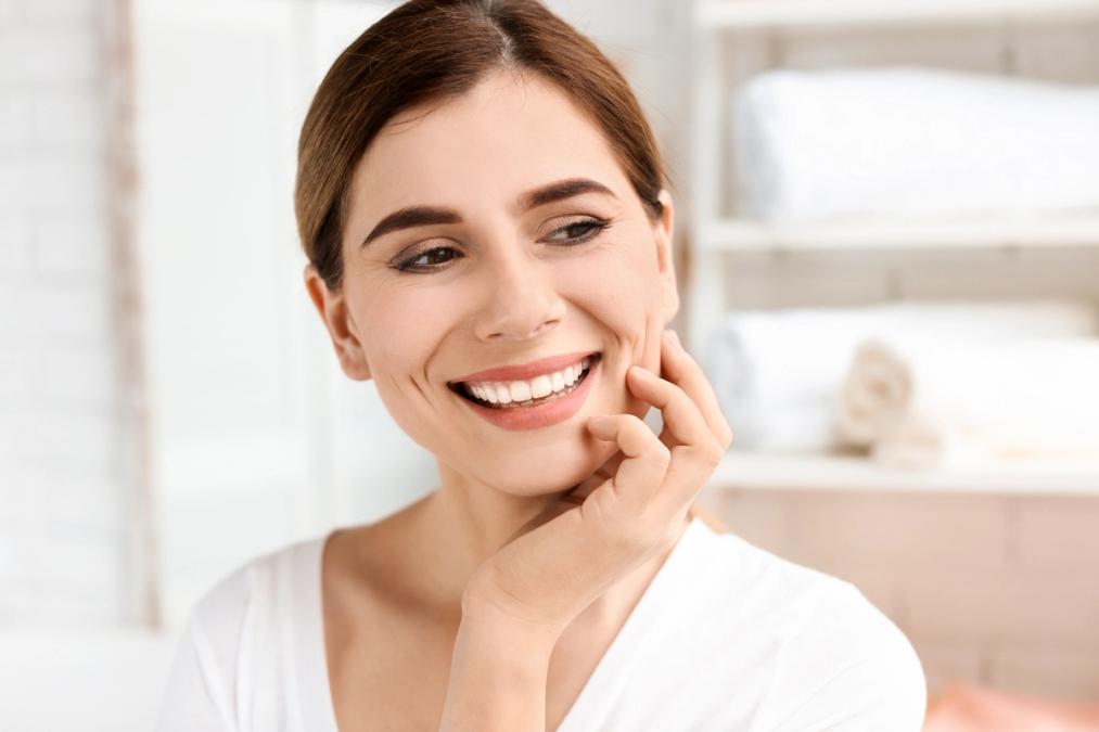 a woman with white teeth is smiling and touching her face.