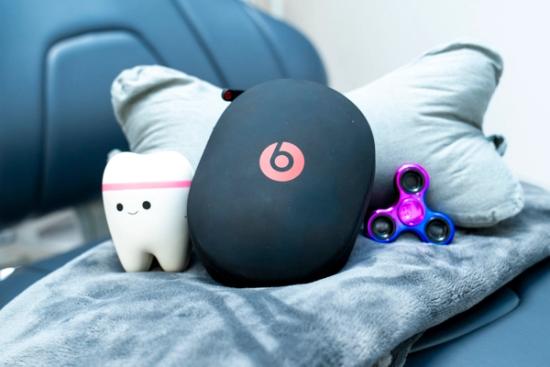 A smiling tooth toy, black Beats headphones case, and a blue and purple fidget spinner on a gray blanket and pillow.