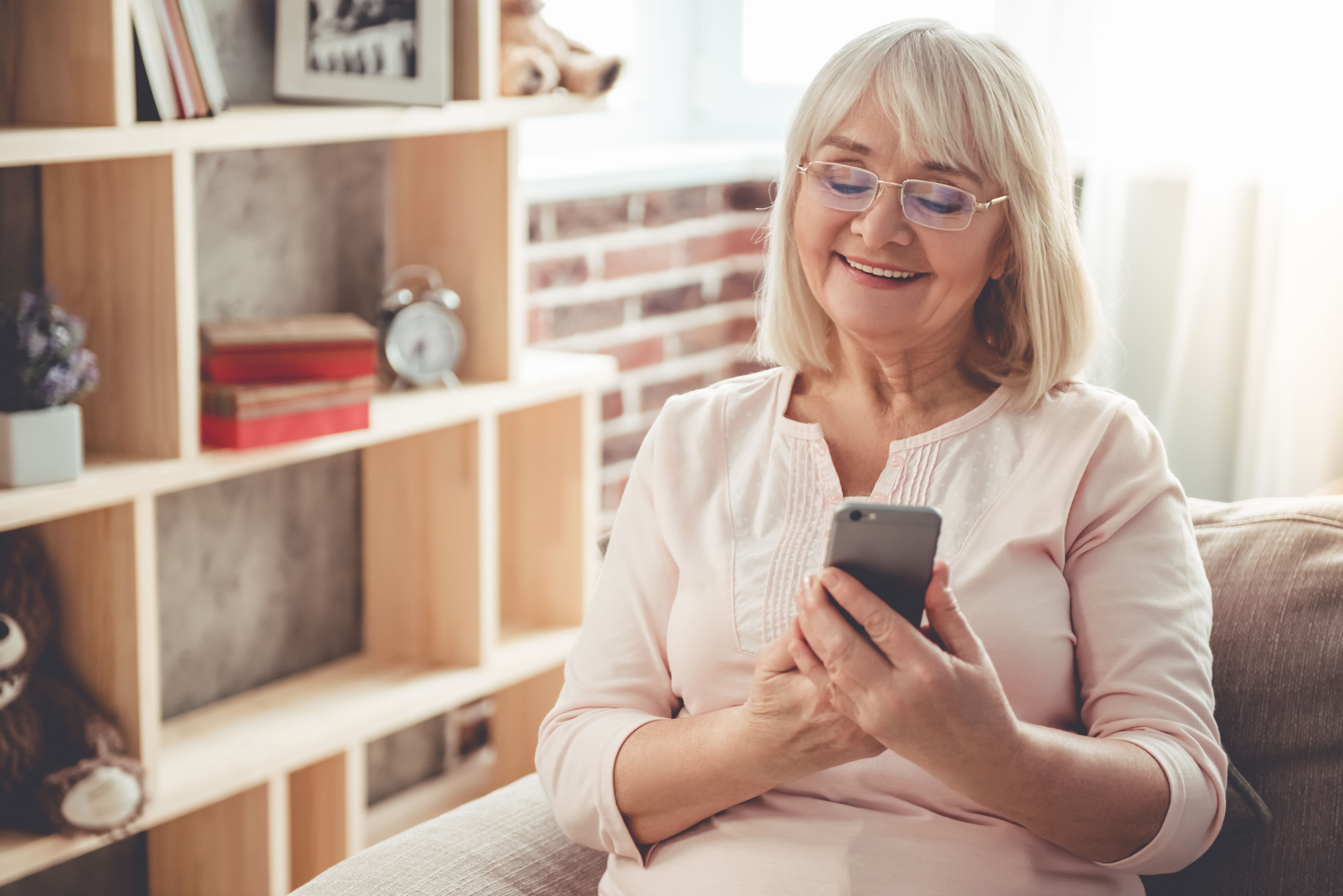 an elderly woman is sitting on a couch using a cell phone .