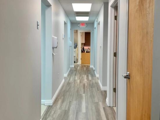 a long hallway in a dental office with wooden floors and a red exit sign .