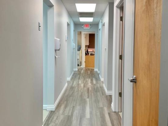 a long hallway in a dental office with wooden floors and a red exit sign .