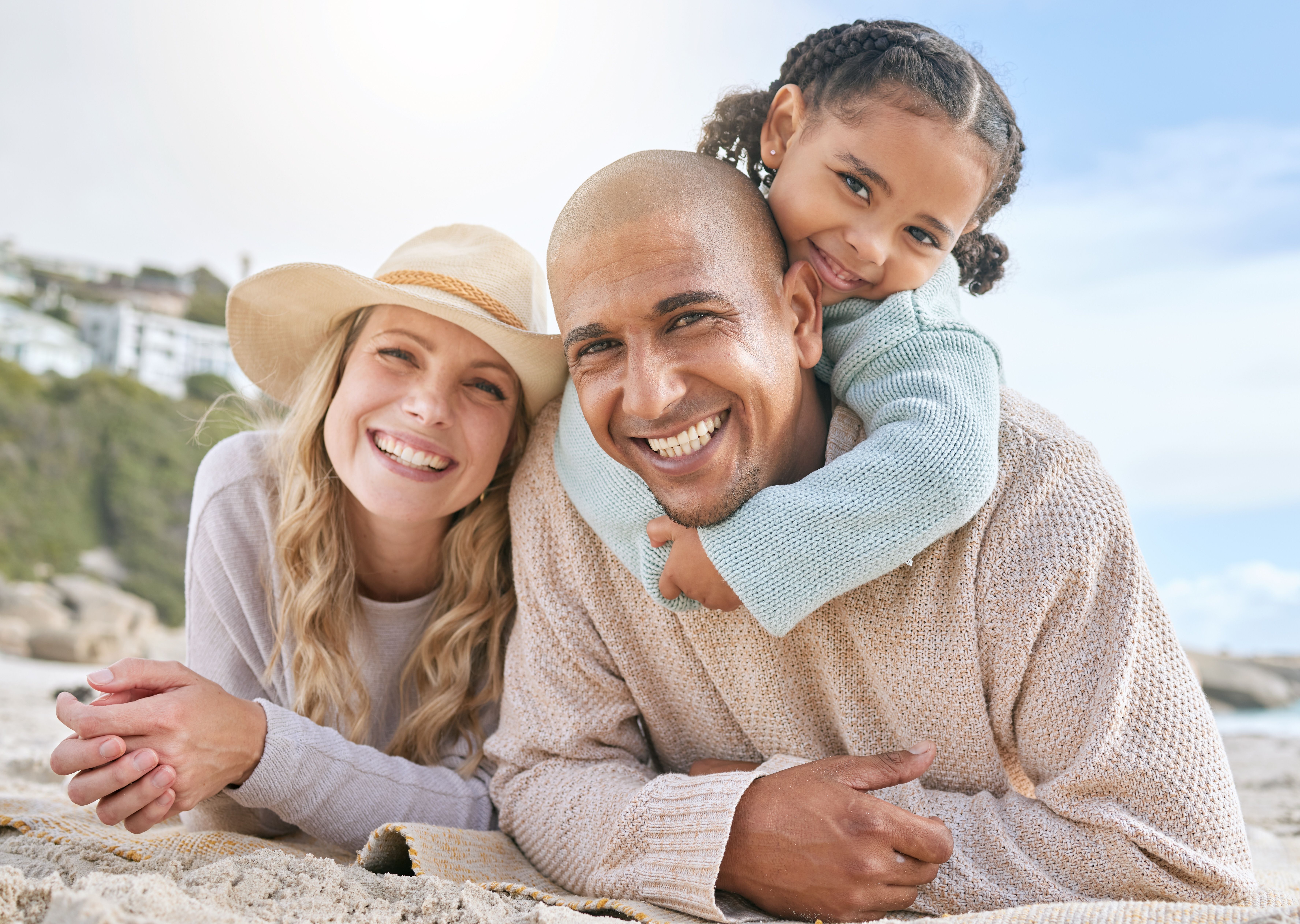 a man and woman are laying on a blanket on the beach with a little girl on their shoulders .