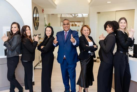 a man in a suit and tie is standing next to a group of women and giving a thumbs up .