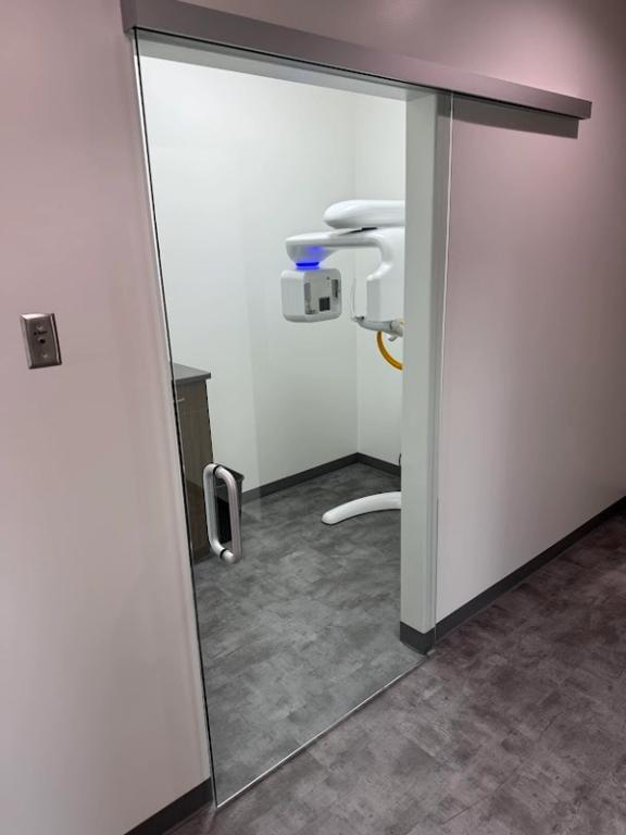 Modern dental panoramic X-ray machine visible through a clear glass sliding door.