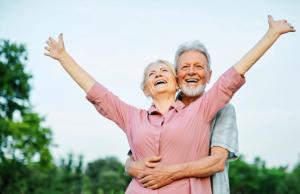 Joyful senior couple laughing, the woman raising her arms while embraced by the man.