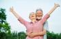 Happy elderly couple embracing with the woman raising her arms in joy.