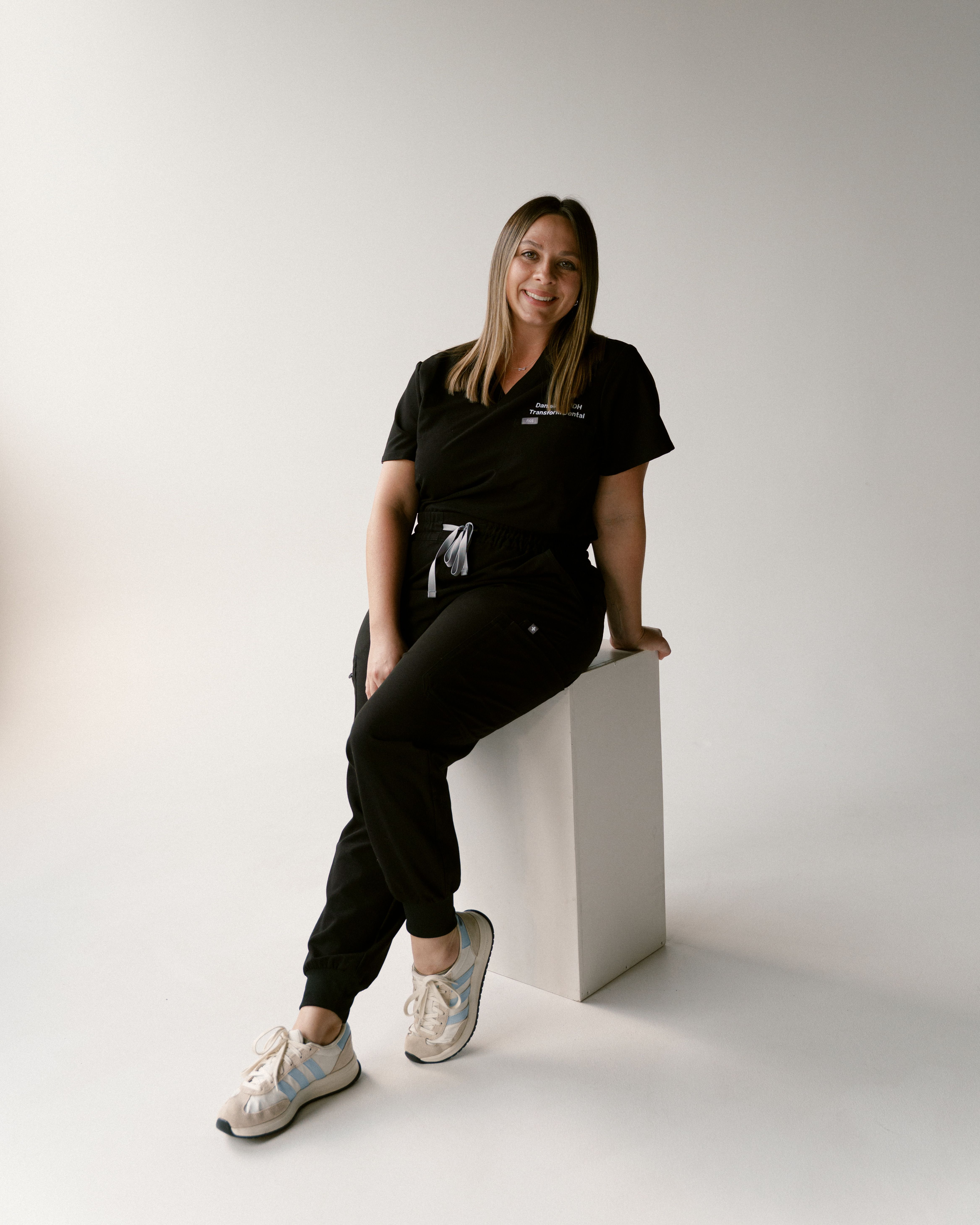 a woman in a black scrub top sits on a white cube