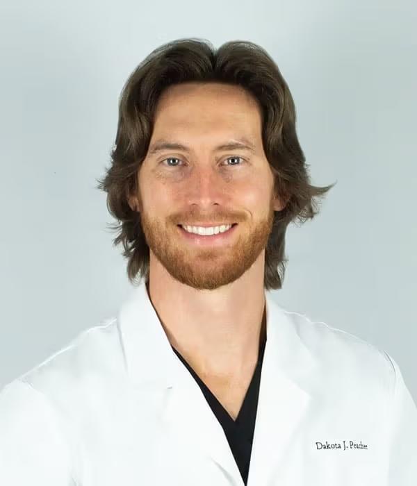 Headshot of Dakota J. Preacher, a smiling man with brown hair and beard wearing a white lab coat.