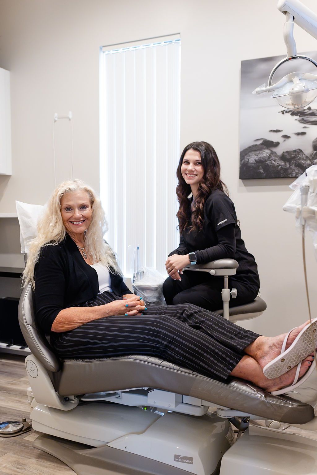 a woman is sitting in a dental chair next to another woman .