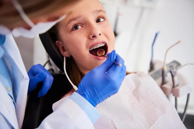 a young girl with braces is having her teeth examined by a dentist .
