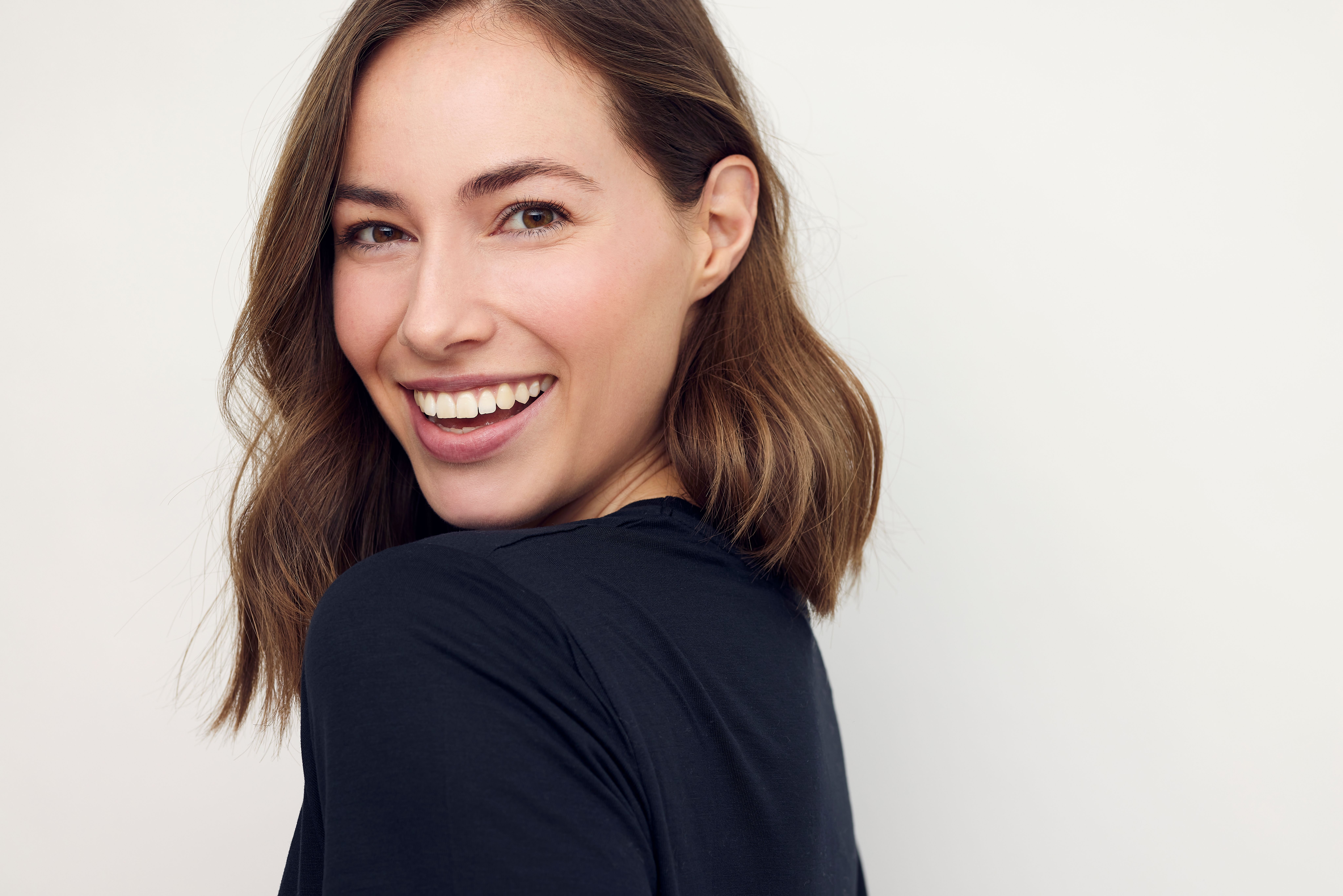 a woman is smiling and looking over her shoulder at the camera .