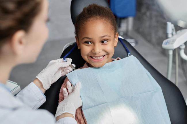Smiling girl in a dental chair with a dentist placing a bib.