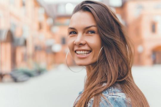a woman with long hair and hoop earrings is smiling and looking at the camera .