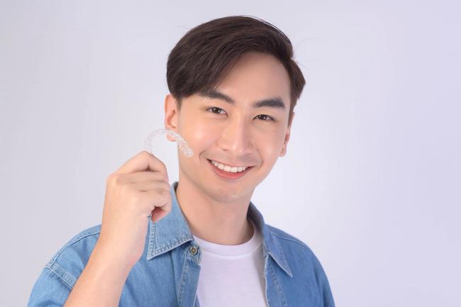 a young man is holding a clear brace on his teeth .