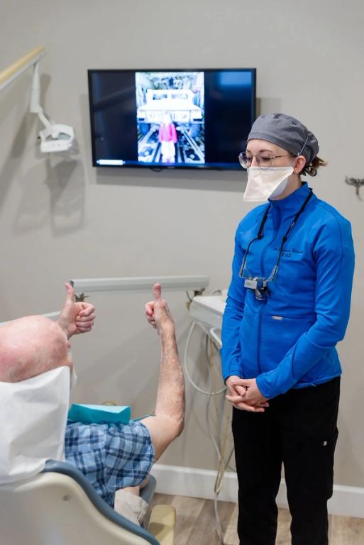 a dentist wearing a mask and a blue jacket talks to a patient