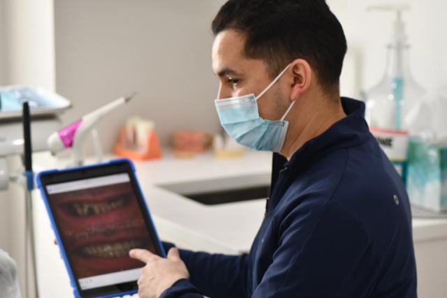 a dentist wearing a mask is looking at a tablet .