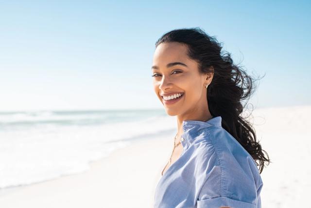 a woman is smiling on the beach and looking at the camera .