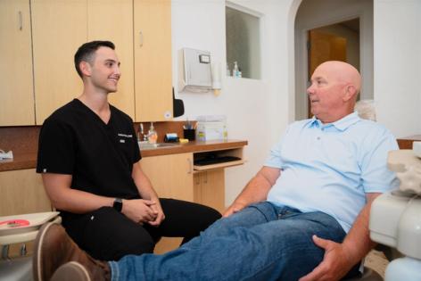 a man is sitting in a dental chair talking to a dentist .