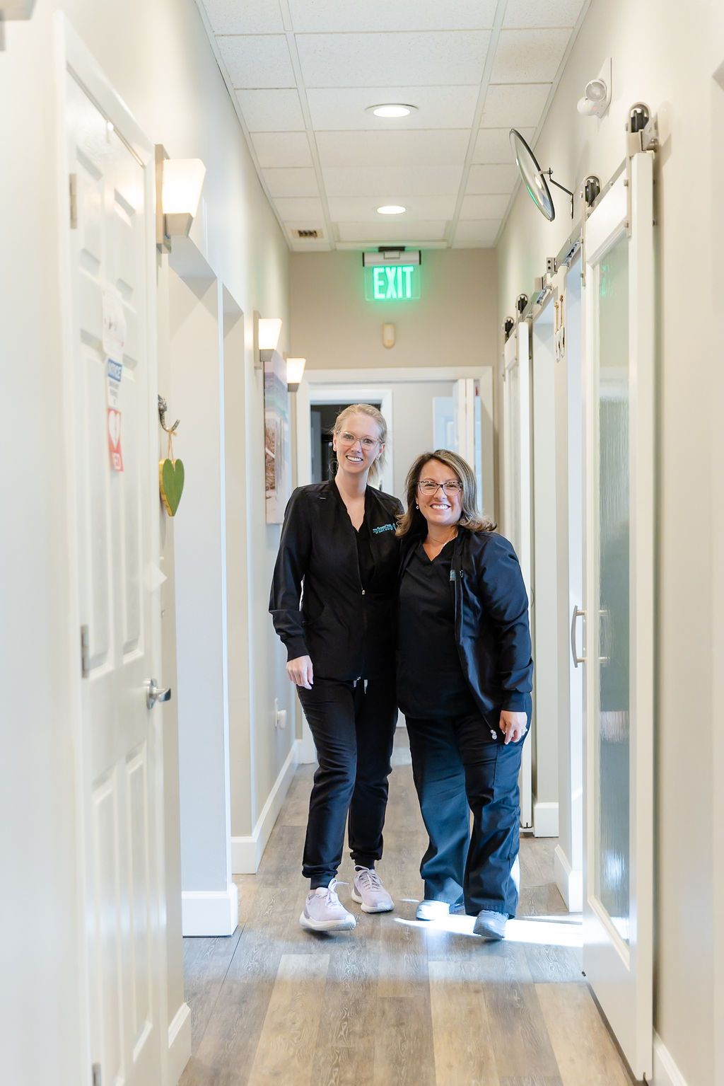 two women are walking down a hallway with a green exit sign above them