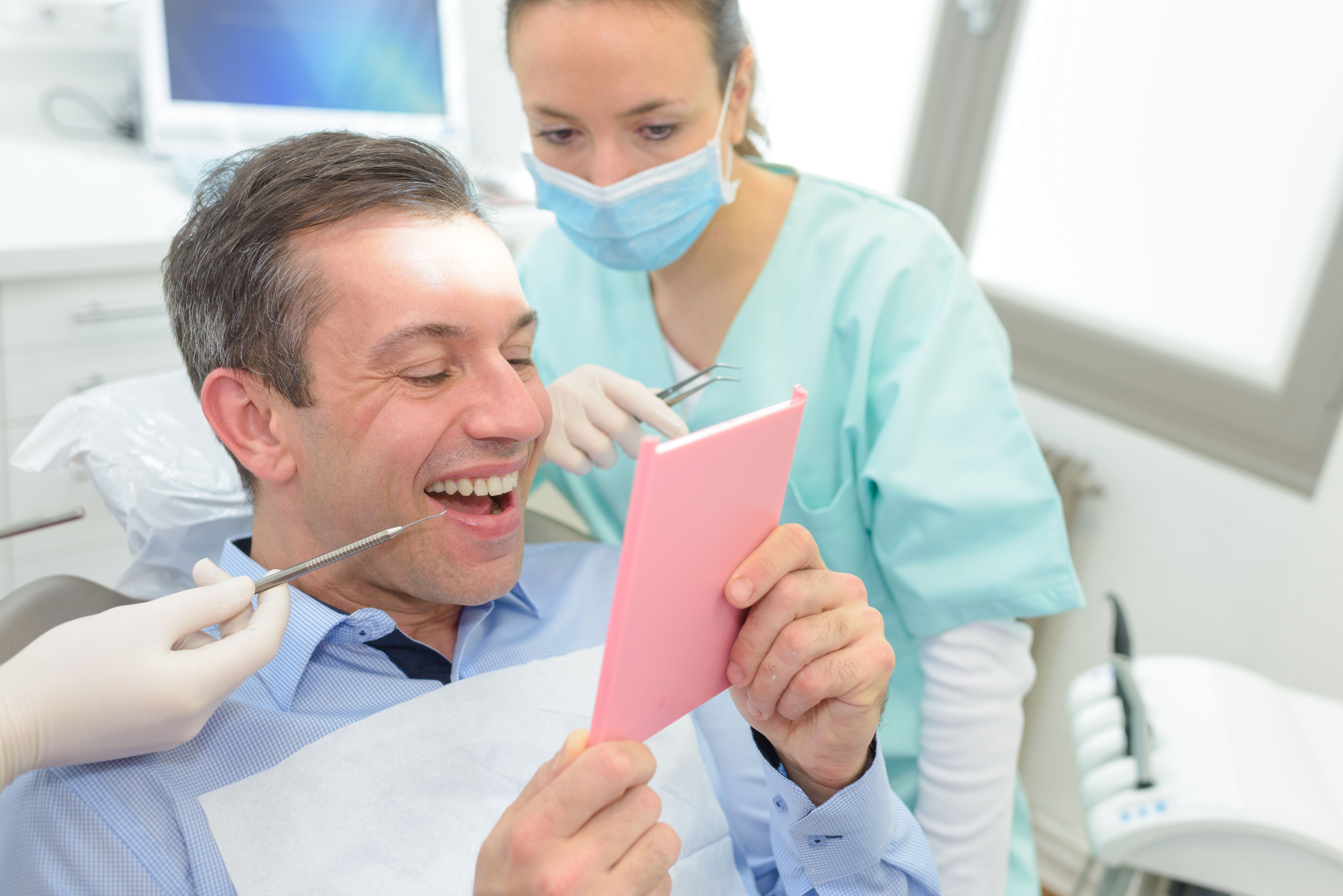 Man smiling at his teeth in a mirror at the dentist's office.