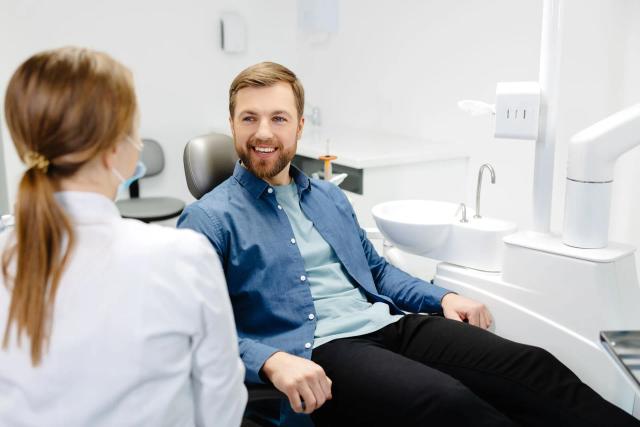 a man is sitting in a dental chair talking to a dentist .