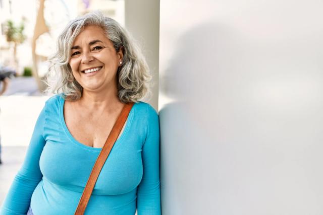 a woman with gray hair is leaning against a wall and smiling .