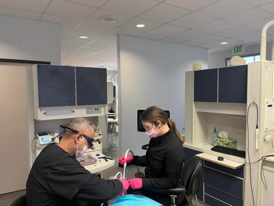 a dentist and a dental assistant are working on a patient 's teeth in a dental office .