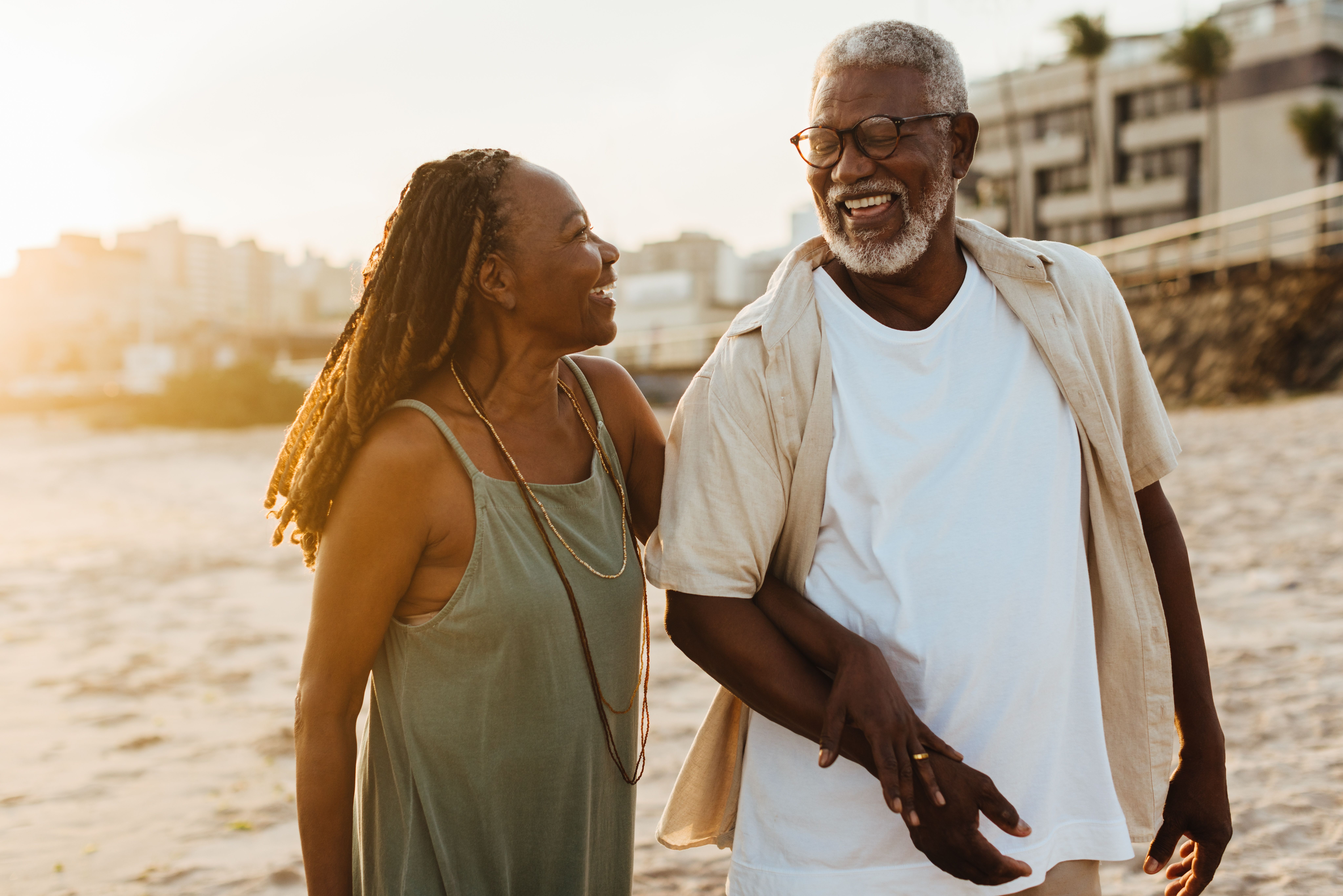 an elderly couple is walking on the beach at sunset .