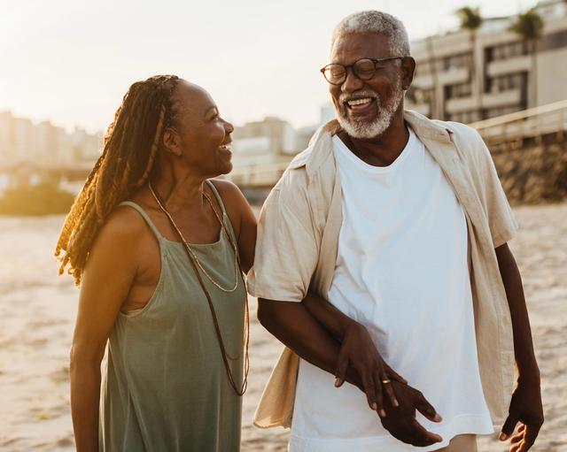an elderly couple is walking on the beach at sunset .