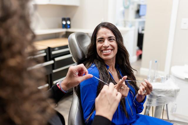 a woman is sitting in a dental chair while a dentist is flossing her teeth .