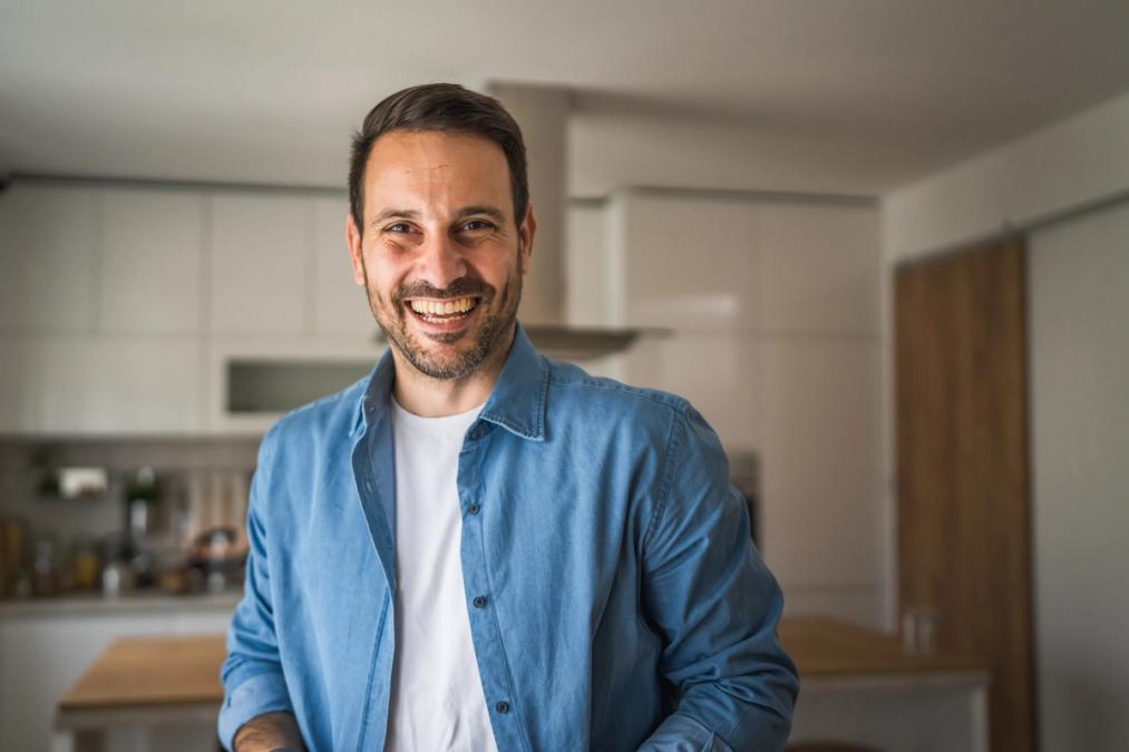 a man in a blue shirt is smiling in a kitchen .