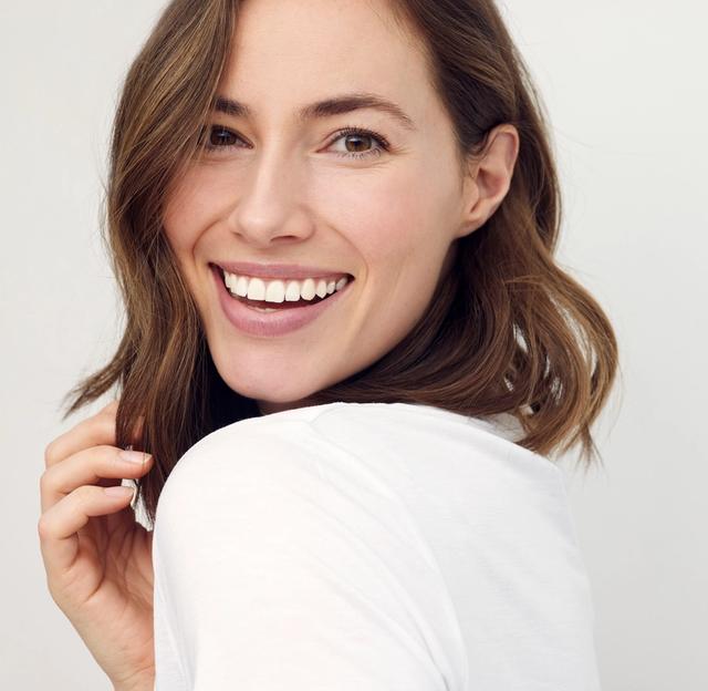 a woman is smiling and looking over her shoulder at the camera .