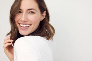 A smiling woman with brown, wavy hair looks over her shoulder.