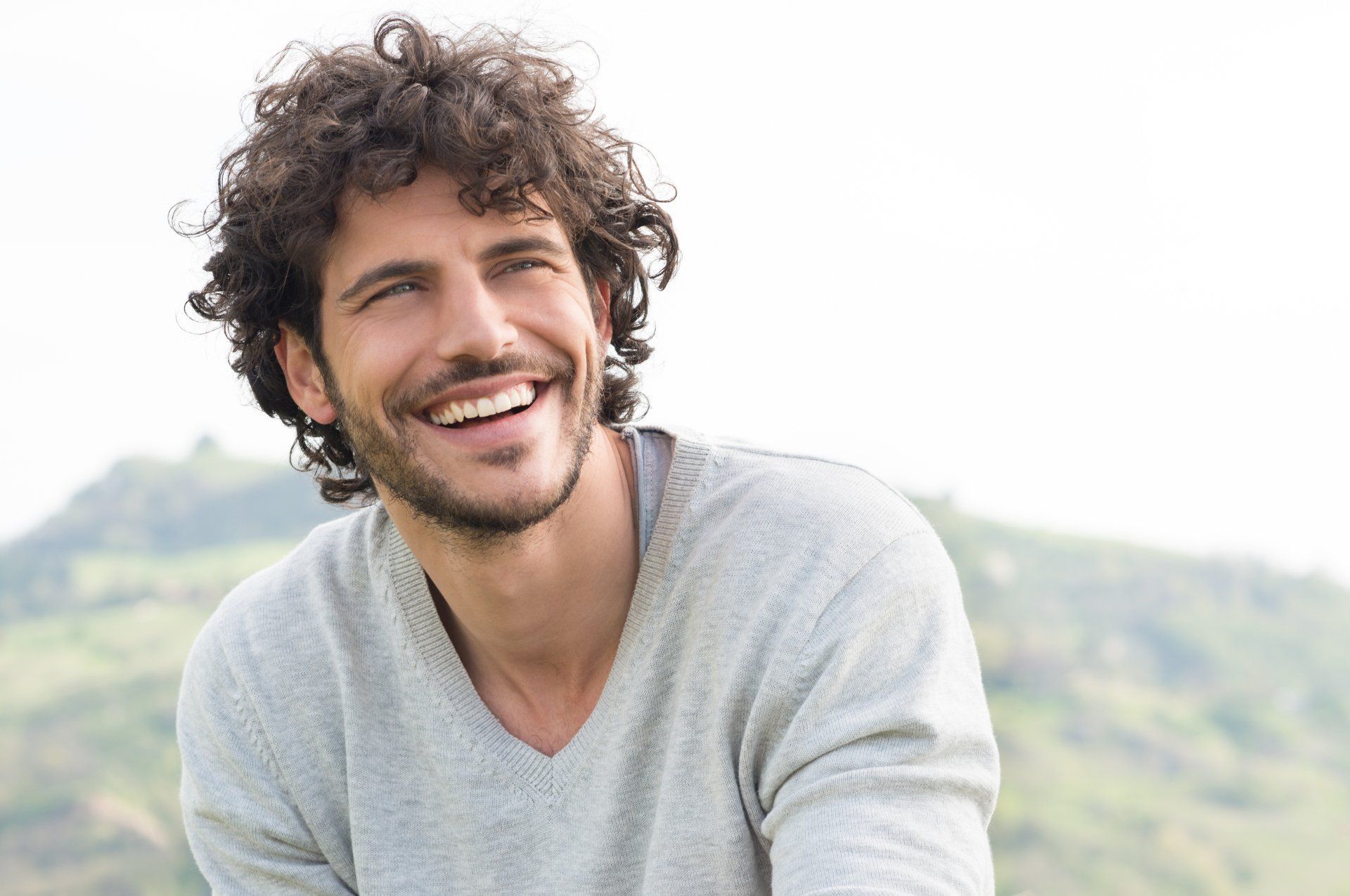 a man with curly hair and a beard is smiling and looking at the camera .