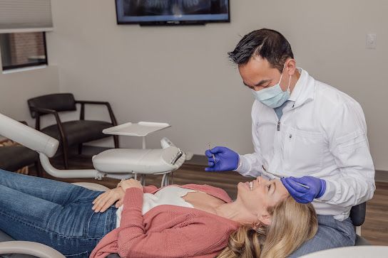 a woman is laying in a dental chair while a dentist examines her teeth .