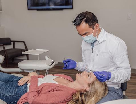 a woman is laying in a dental chair while a dentist examines her teeth .