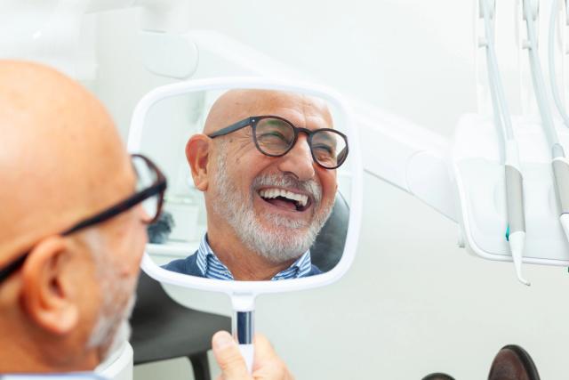 a man is looking at his smile in a mirror at the dentist .