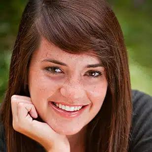 a young woman with freckles is smiling with her hand on her chin .